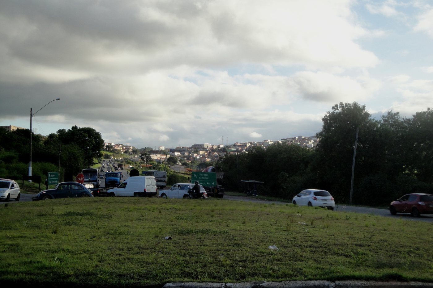 Área de parada à beira da estrada com veículos estacionados e a cidade ao fundo